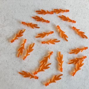May include: A collection of 19 orange plastic flame pieces. The flames are in various shapes and sizes, and they are all made of a translucent plastic.