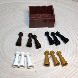 May include: A collection of brown, black, white, and gold toy parts, including a rectangular brown block and several cylindrical pieces. The parts are arranged on a light brown, wood-grain surface.