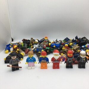 May include: A collection of assorted Lego minifigures, including a construction worker, a police officer, a Santa Claus, a woman with pink and blue clothing, a man with a black robe and glasses, and a man with a red helmet and black suit.