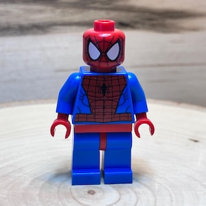 Op de afbeelding: Een rood en blauw Lego minifiguur van Spiderman. De figuur heeft een rood hoofd met een wit masker en een blauwe torso met een rood spinnenwebontwerp.