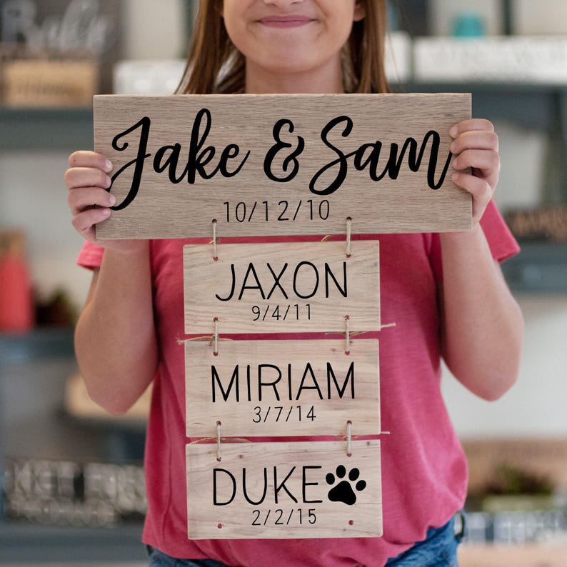 A woman holding a wooden sign featuring her family names and dates.