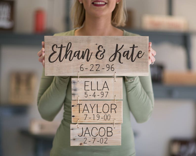 A cute mom holding a family list sign with the names and dates of birth of her children and her and her husband's wedding date.