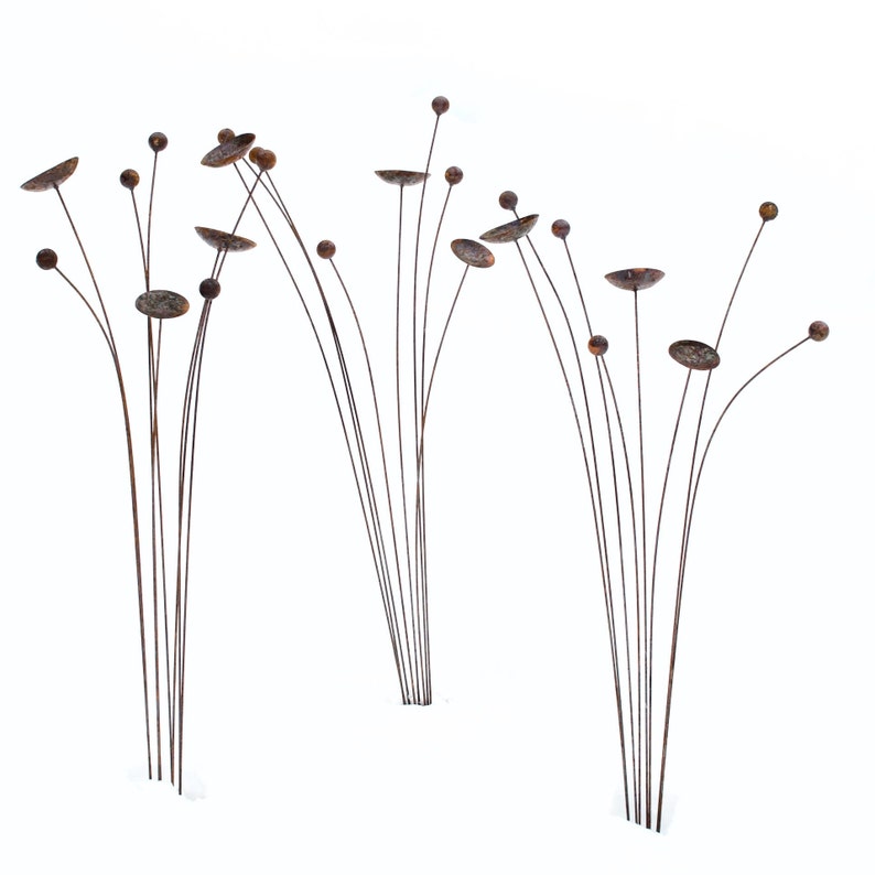 Three sets of metal kinetic garden art with rust patina creates an impact and mimics natural plantings.