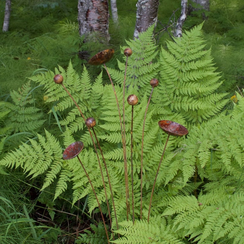 Metal kinetic garden art with rust patina in fern garden.