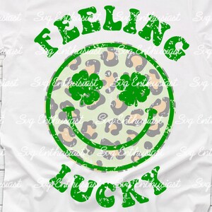 Peut inclure: Un t-shirt blanc avec un graphique délavé vert et blanc qui dit "Feeling Lucky" avec un trèfle vert et un smiley imprimé léopard.