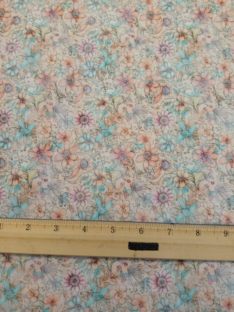 May include: A beige fabric with a floral pattern in shades of pink, blue, and brown. The fabric has a vintage, watercolor look. A ruler is placed on the fabric to show the scale.