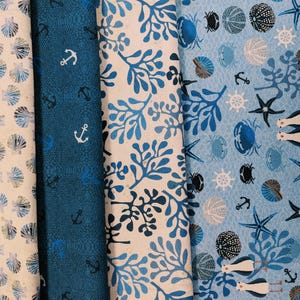 May include: A collection of four fabric swatches with nautical-themed patterns. Designs include seashells, anchors, and marine life in shades of blue and white. The fabrics are suitable for various craft projects.