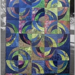 May include: A patchwork quilt with a repeating pattern of blue, green, and gold crescent shapes. The quilt features the text "Blue Onion" at the top and "Saginaw St Quilts" at the bottom right.