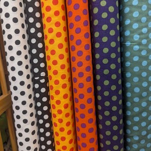 May include: A collection of fabric rolls with polka dot patterns. The rolls display various colors, including white with black dots, black with white dots, yellow with red dots, orange with purple dots, purple with green dots, and teal with light blue dots.