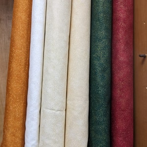 May include: Six rolls of fabric with a subtle gold glitter pattern. The fabric rolls are in the colors orange, white, cream, beige, green, and burgundy.