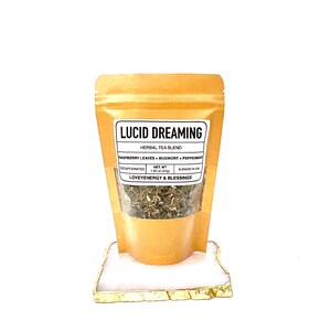 May include: A brown paper pouch with a white label that reads "LUCID DREAMING HERBAL TEA BLEND RASPBERRY LEAVES MUGWORT+PEPPERMAT DECAFFEINATED NET WT 1.30 oz (37g) BLENDED IN USA LOVEYENERGY & BLESSINGS". The pouch contains dried herbs.