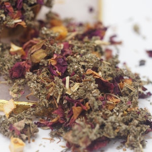 May include: A close-up of a blend of dried herbs and flowers, including rose petals, dried leaves, and small pieces of fruit. The mixture is a light brown color with hints of pink and orange.