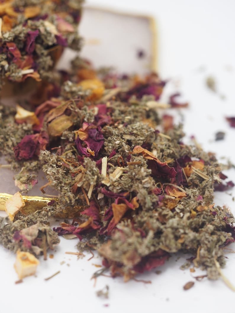 May include: A close-up of a blend of dried herbs and flowers, including rose petals, dried leaves, and small pieces of fruit. The mixture is a light brown color with hints of pink and orange.