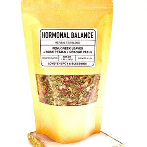 May include: A brown paper bag of herbal tea blend, labeled "HORMONAL BALANCE." The label lists ingredients: fenugreek leaves, rose petals, and orange peels. The bag contains a visible mix of dried herbs and flowers. The net weight is 1.80 oz (50g).
