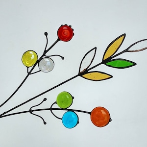 Puede incluir: Una rama decorativa de metal con orbes y hojas de vidrio de colores. Los orbes son amarillos, transparentes, verdes, azules y naranjas. Las hojas son amarillas, verdes y transparentes. El metal es negro.