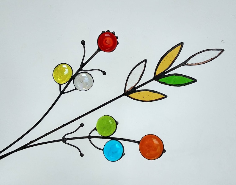 Puede incluir: Una rama decorativa de metal con orbes y hojas de vidrio de colores. Los orbes son amarillos, transparentes, verdes, azules y naranjas. Las hojas son amarillas, verdes y transparentes. El metal es negro.