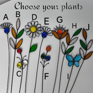 Puede incluir: Una selecci&oacute;n de estacas decorativas para jard&iacute;n con acentos de vidrio de colores. Los dise&ntilde;os incluyen flores, hojas y una mariposa. El texto "Choose your plants" est&aacute; en la parte superior. Cada estaca tiene un tallo de metal negro.