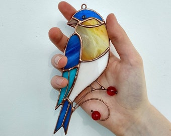 May include: A stained glass bird ornament with blue, white, and yellow glass pieces. The bird has a copper wire frame and red glass beads hanging from the bottom.