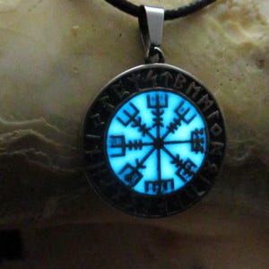 May include: A silver necklace with a round pendant featuring a glowing blue compass with Norse runes around the edge.