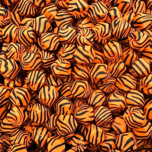 May include: A close-up of a pile of orange and black hexagonal beads with a tiger stripe pattern.