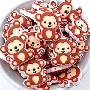 May include: A collection of brown and white silicone monkey charms. The monkeys have a cartoon-like design with big eyes and a smile. The charms are perfect for adding a playful touch to jewelry, keychains, or other crafts.