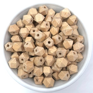 May include: A bowl filled with natural wood beads. The beads are in the shape of a diamond with a hole in the center. The beads are a light brown color.