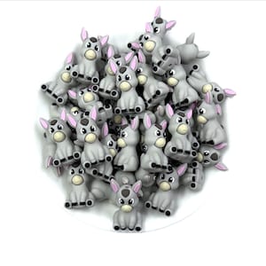 May include: A collection of gray donkey-shaped embellishments with pink ears and black hooves. These small, cartoonish figures are arranged in a pile, perfect for crafting or adding a whimsical touch to various projects. The donkeys have a friendly expression.