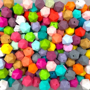 May include: A collection of colorful, geometric silicone beads in various shades of pink, purple, green, orange, yellow, and blue. These beads are designed with multiple facets and are likely used for crafting or jewelry making.