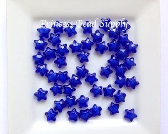 May include: A collection of blue star-shaped glass beads. The beads are translucent and have a slightly iridescent finish.