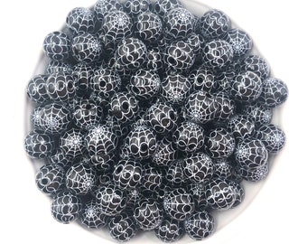 May include: A bowl filled with black and white silicone beads with a spiderweb design. The beads are oval shaped and have a glossy finish.