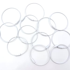 May include: A set of ten white metal key rings. The rings are all the same size and are arranged in a pile.