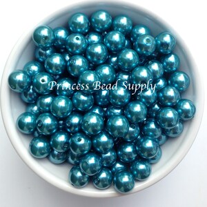May include: A bowl filled with teal blue pearl-like beads. The beads are smooth and shiny, and they have a metallic finish. The beads are all the same size and shape.