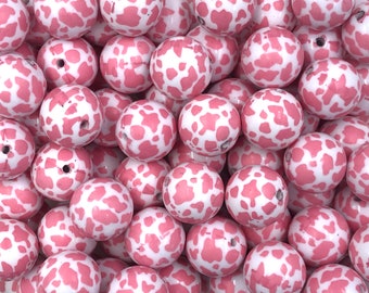 May include: A close-up of a pile of pink and white cow print beads. The beads are round and have a smooth, glossy finish.