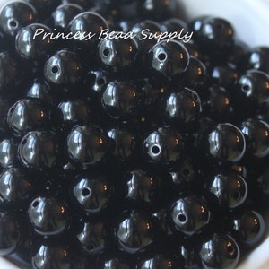 May include: A bowl filled with black round beads. The beads are shiny and have a small hole in the center. The beads are arranged in a random pattern.