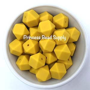 May include: A bowl filled with yellow silicone beads. The beads are shaped like a hexagon with rounded edges. The beads are for making jewelry or other crafts.