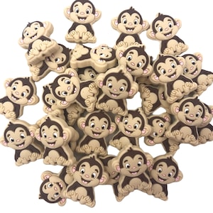 May include: A large group of brown and tan silicone monkey charms. The monkeys have brown eyes, a brown mouth, and a brown tail. They are all smiling.