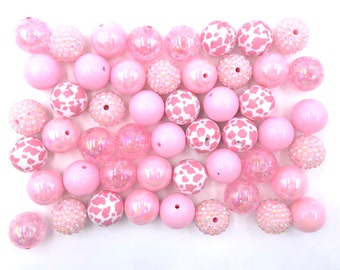 May include: A collection of pink and white chunky beads, some with a cow print pattern, some with glitter, and some with a smooth finish.