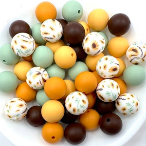May include: A collection of silicone beads in various colors, including brown, green, yellow, and white. Some of the beads have a sunflower pattern.