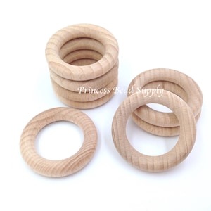 May include: A group of wooden rings, some stacked on top of each other, and some laying flat. The rings are unfinished and have a natural wood color.  The rings are approximately 2 inches in diameter.