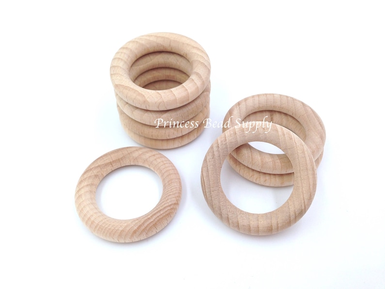 May include: A group of wooden rings, some stacked on top of each other, and some laying flat. The rings are unfinished and have a natural wood color.  The rings are approximately 2 inches in diameter.