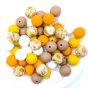 May include: A collection of colorful silicone beads in yellow, brown, and white. Some beads feature a floral pattern with sunflowers and daisies. These beads are perfect for making necklaces, bracelets, or other crafts.