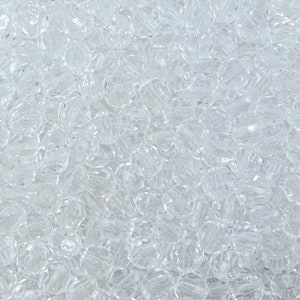 May include: A close-up image of a large quantity of clear glass beads. The beads are small and round, with a slightly faceted surface.
