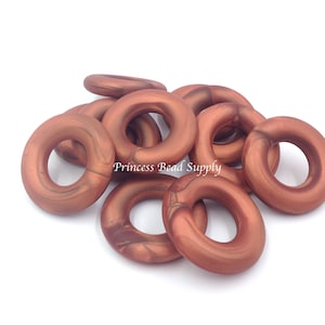 May include: A group of 10 copper-colored polymer clay donut beads. The beads have a marbled effect and are approximately 1 inch in diameter.