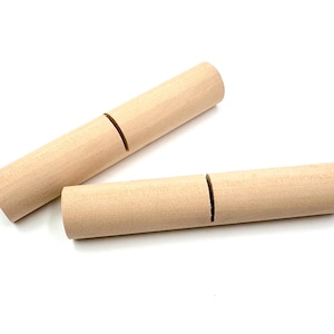 May include: Two unfinished wooden dowels with a single, deep groove cut into each. The dowels are cylindrical and made of light-colored wood. They are lying on a white surface.