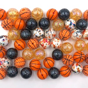 May include: A collection of orange and black basketball-themed beads. The beads are made of plastic and have a variety of designs, including solid orange, solid black, and orange with black speckles.
