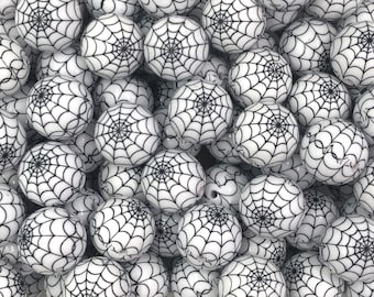 May include: A large pile of white and black spiderweb patterned beads. The beads are round and have a glossy finish.