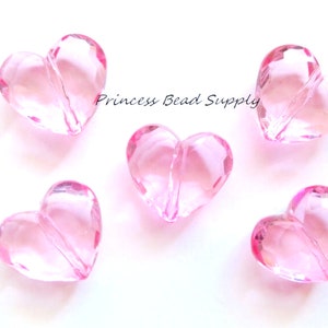 May include: Five pink heart-shaped beads with a hole through the center. The beads are made of clear acrylic and have a faceted design.