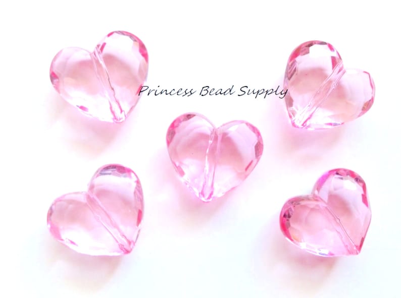 May include: Five pink heart-shaped beads with a hole through the center. The beads are made of clear acrylic and have a faceted design.