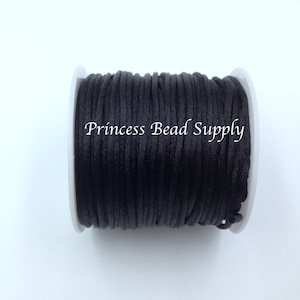 May include: A spool of black cord, wound on a white plastic bobbin. The text "Princess Bead Supply" is printed on the spool.