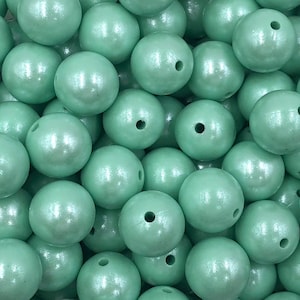 May include: A close-up of a group of light green, pearl-like beads. The beads are smooth and shiny, and they have a slight shimmer to them.